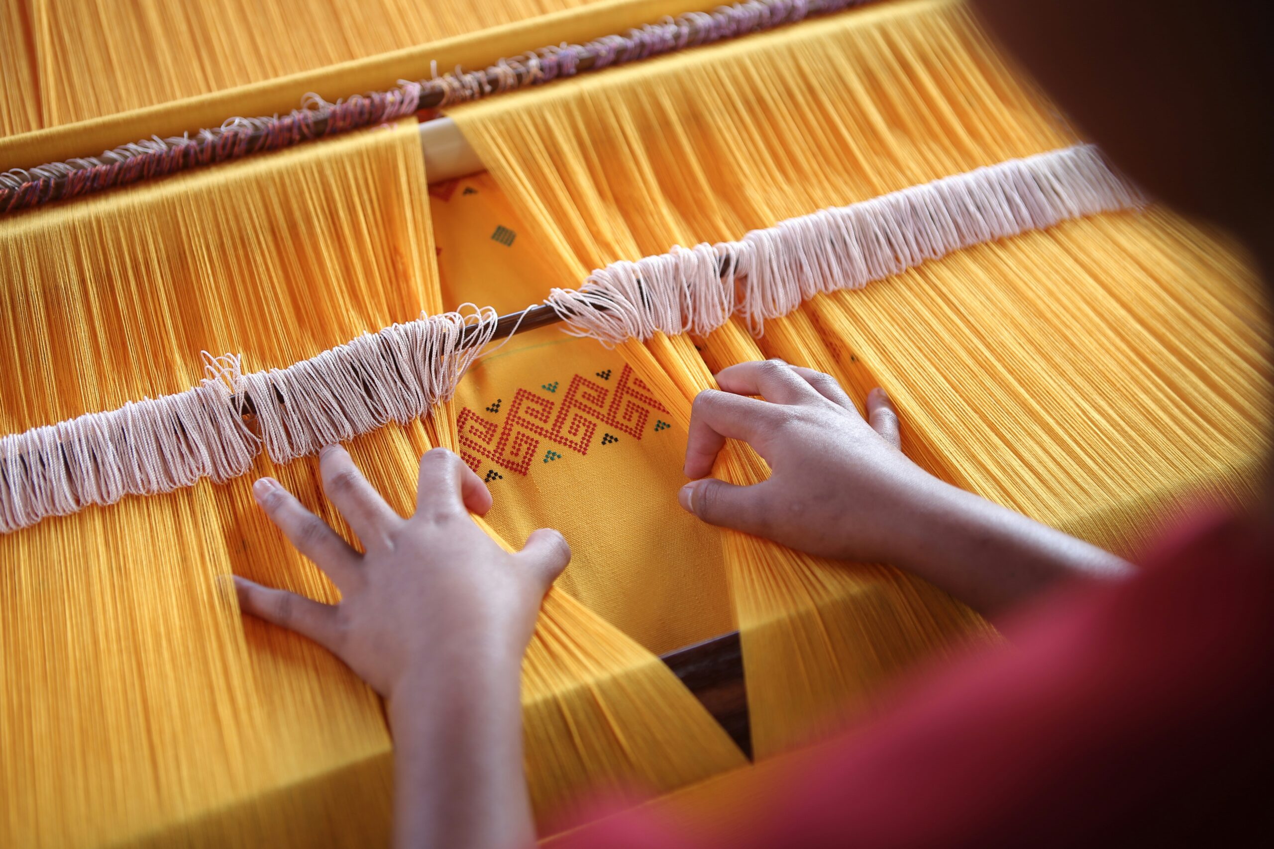 Hands working at a traditional loom weaving vibrant yellow fabric with intricate patterns, demonstrating the craftsmanship involved in kimono textile production