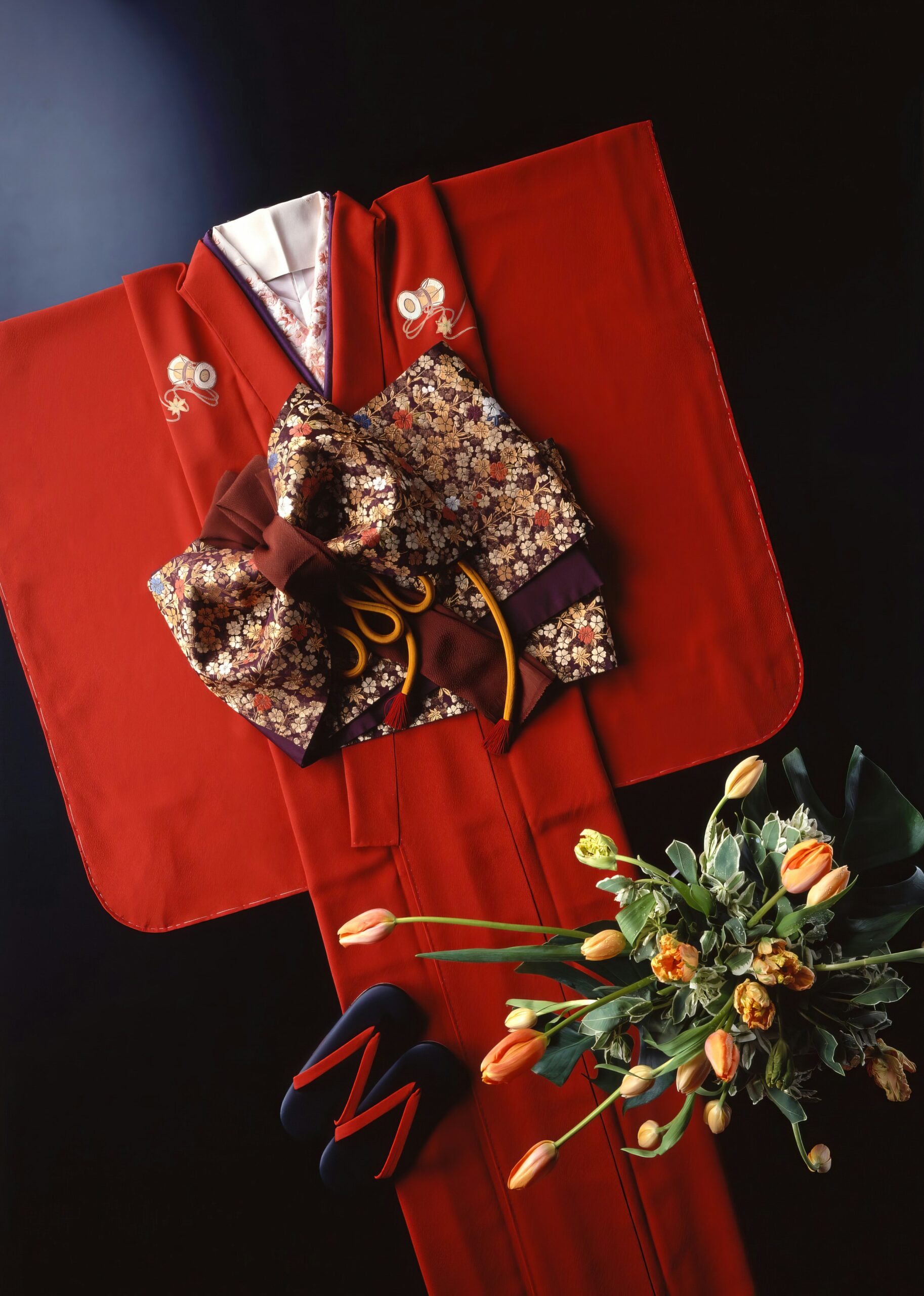Formal red kimono with decorative obi and floral accessories laid flat for display