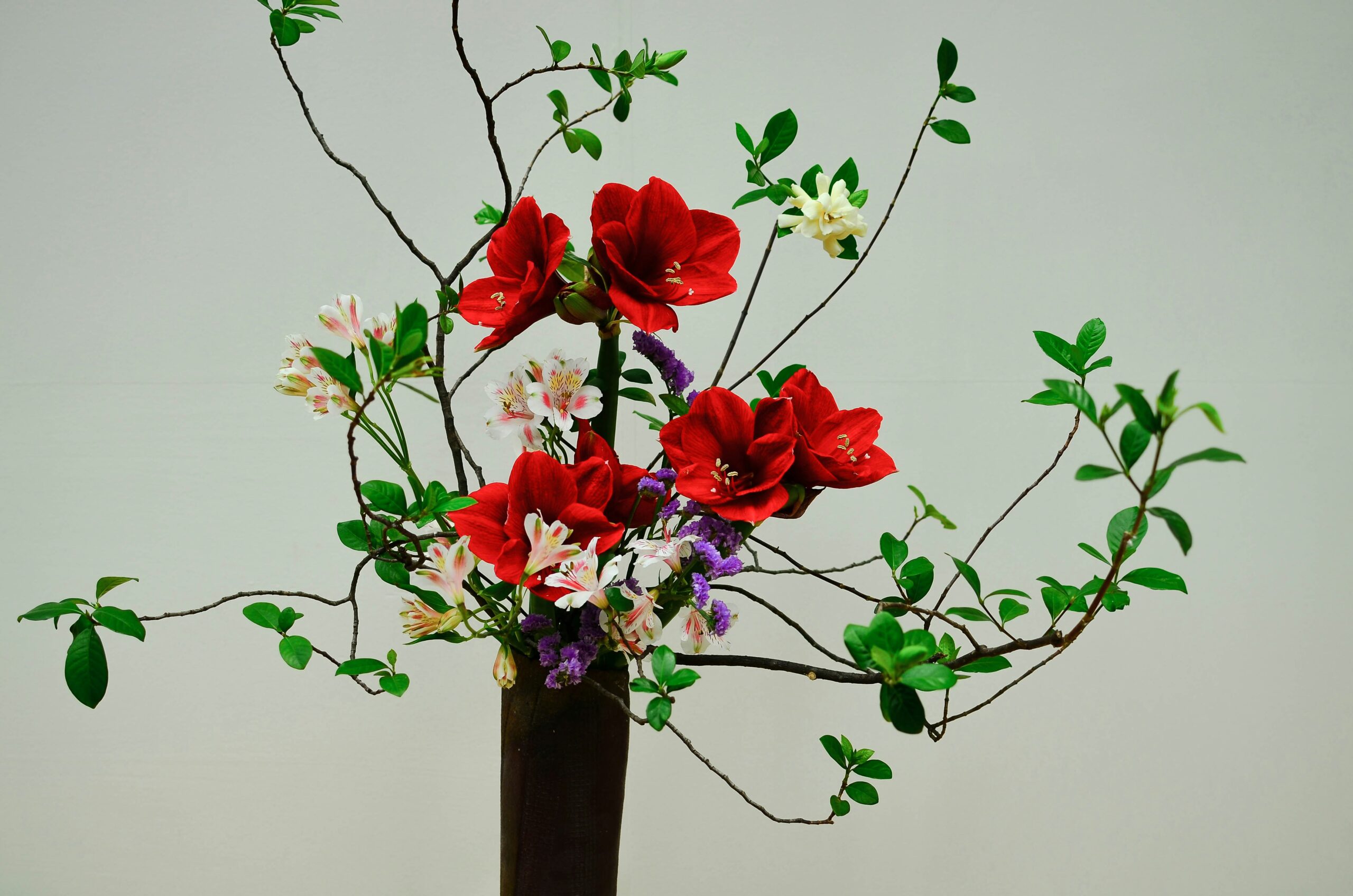 Traditional ikebana flower arrangement with vibrant red flowers, white blooms, and green foliage, demonstrating the Japanese art of seasonal expression through natural elements