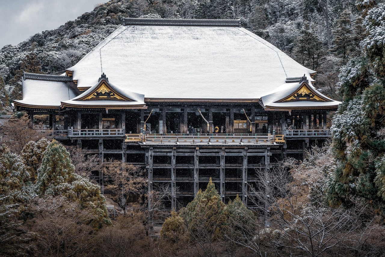 Snow-covered Japanese temple with traditional architecture featuring wooden structures and curved roofs with golden accents amidst a winter landscape