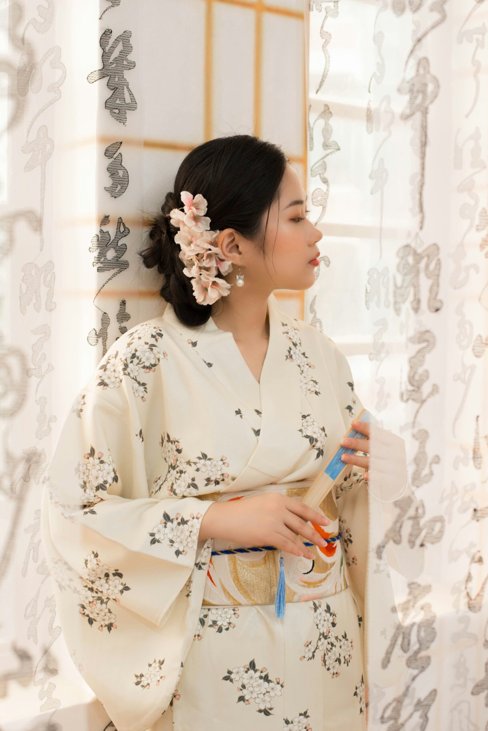 Woman in a light-colored kimono with floral patterns, elegantly styled with cherry blossoms in her hair, representing the delicate beauty of traditional Japanese attire