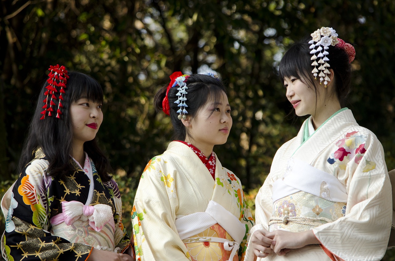 Three women wearing colorful traditional kimonos with elaborate floral patterns and traditional hair ornaments, representing the seasonal beauty of Japanese fashion traditions