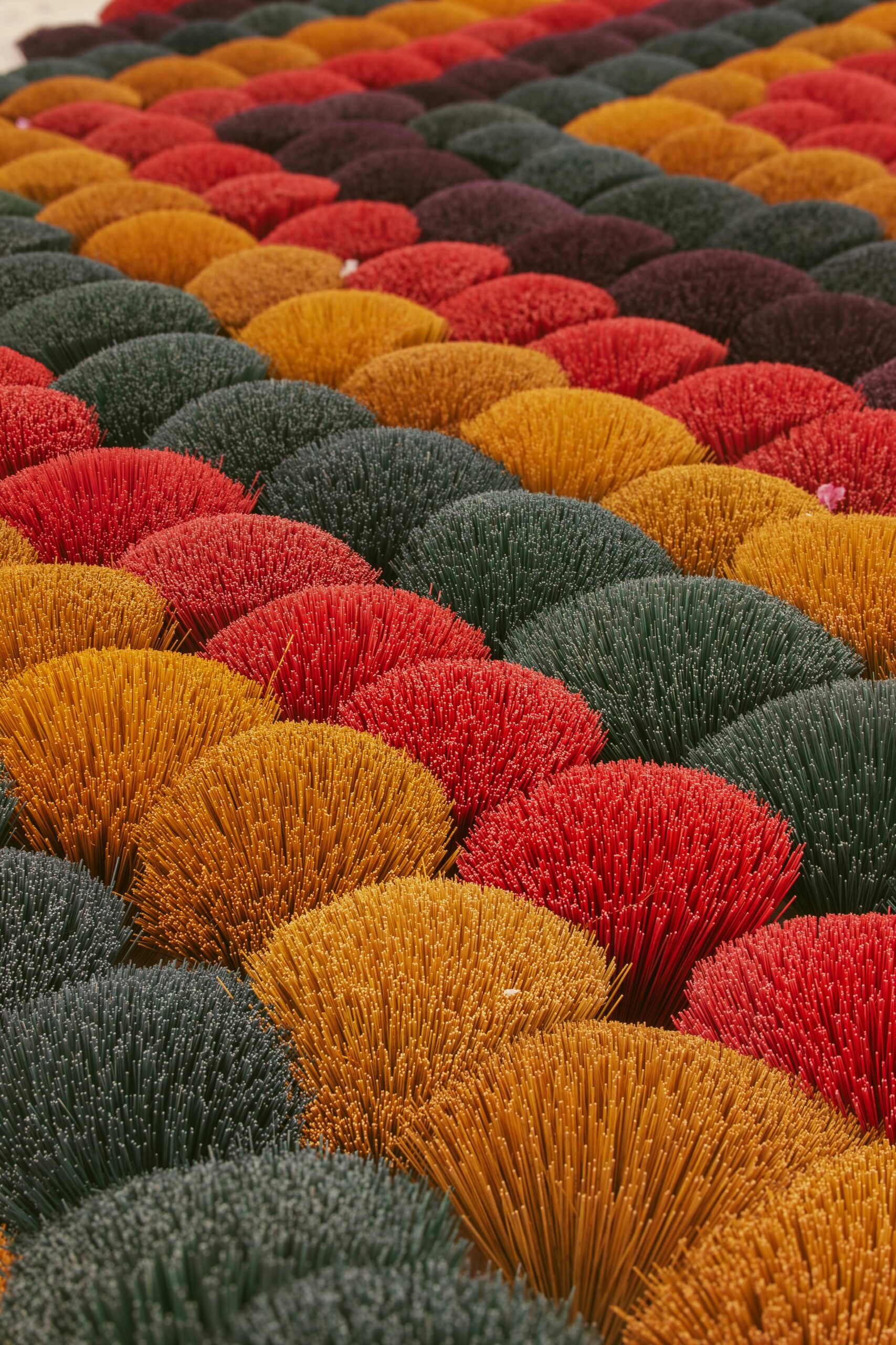 Colorful array of incense sticks in vibrant red, orange, yellow, and green arranged in neat rows, representing the rich color palette used in traditional Japanese arts