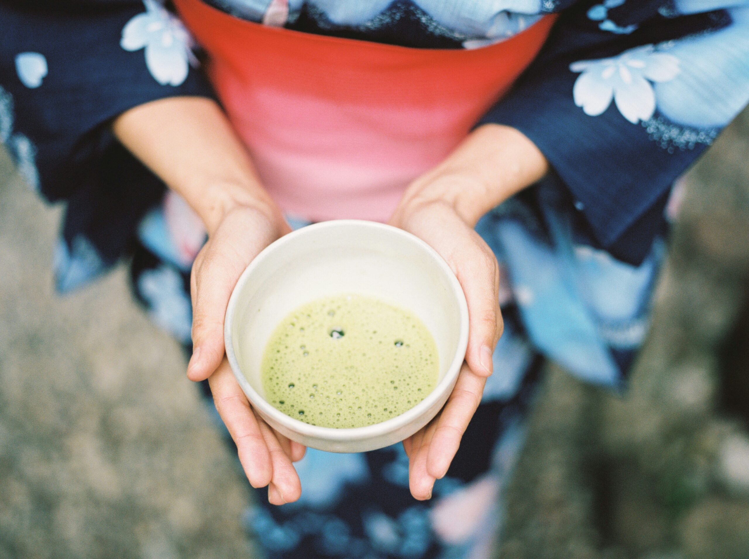 Person in a blue floral kimono holding a bowl of matcha tea
