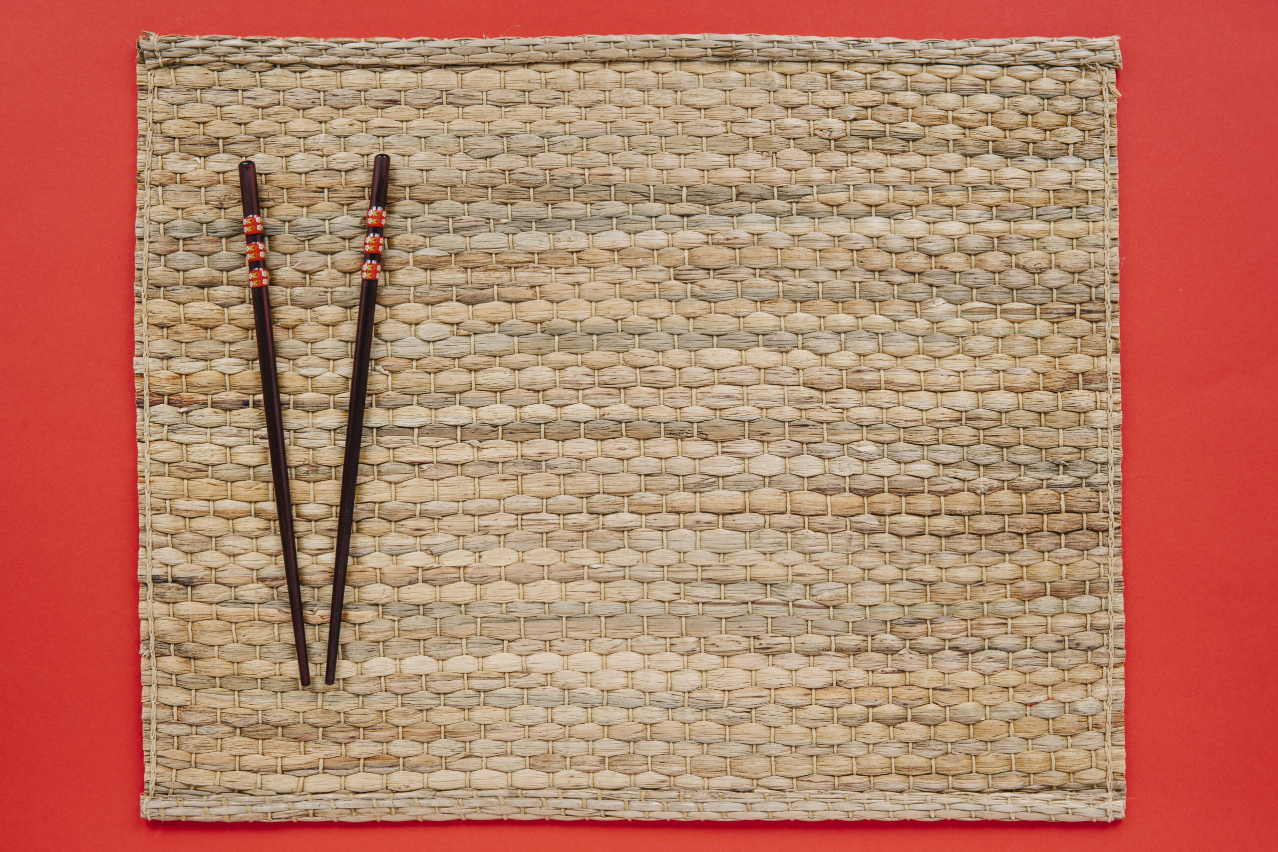 Traditional Japanese chopsticks on a woven bamboo mat against a red background