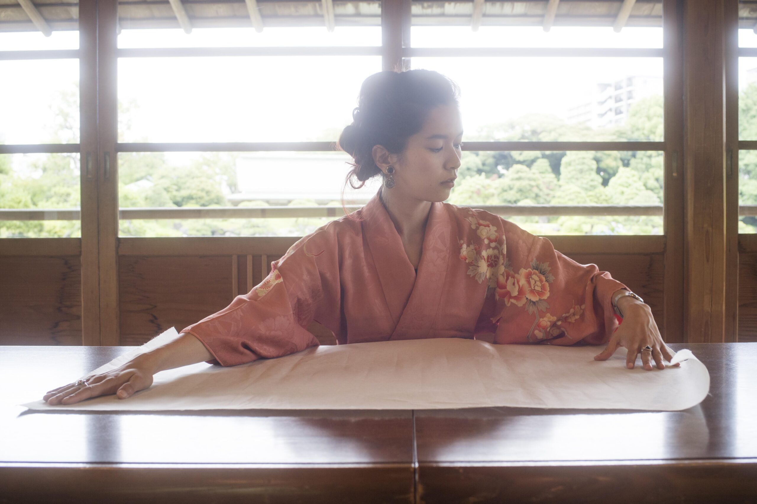 Person in a peach-colored kimono seated at a traditional table preparing for a ceremony