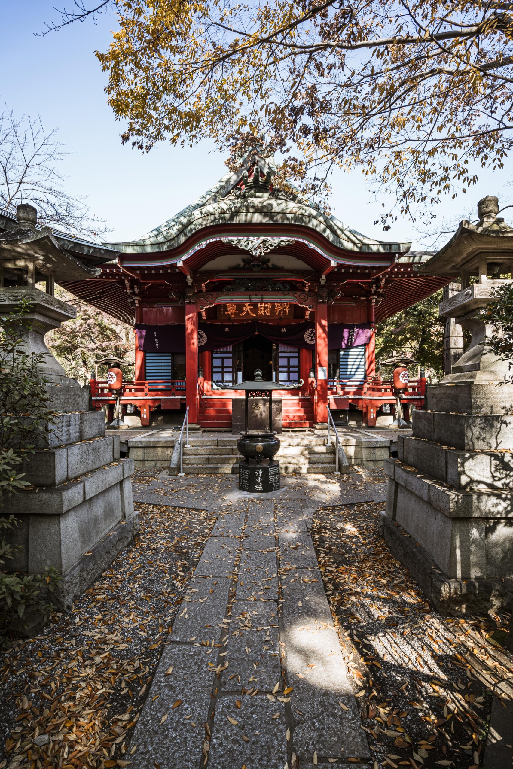 Traditional red Japanese shrine temple with curved rooflines and ornate details surrounded by autumn foliage and stone lanterns, perfect backdrop for kimono photography sessions