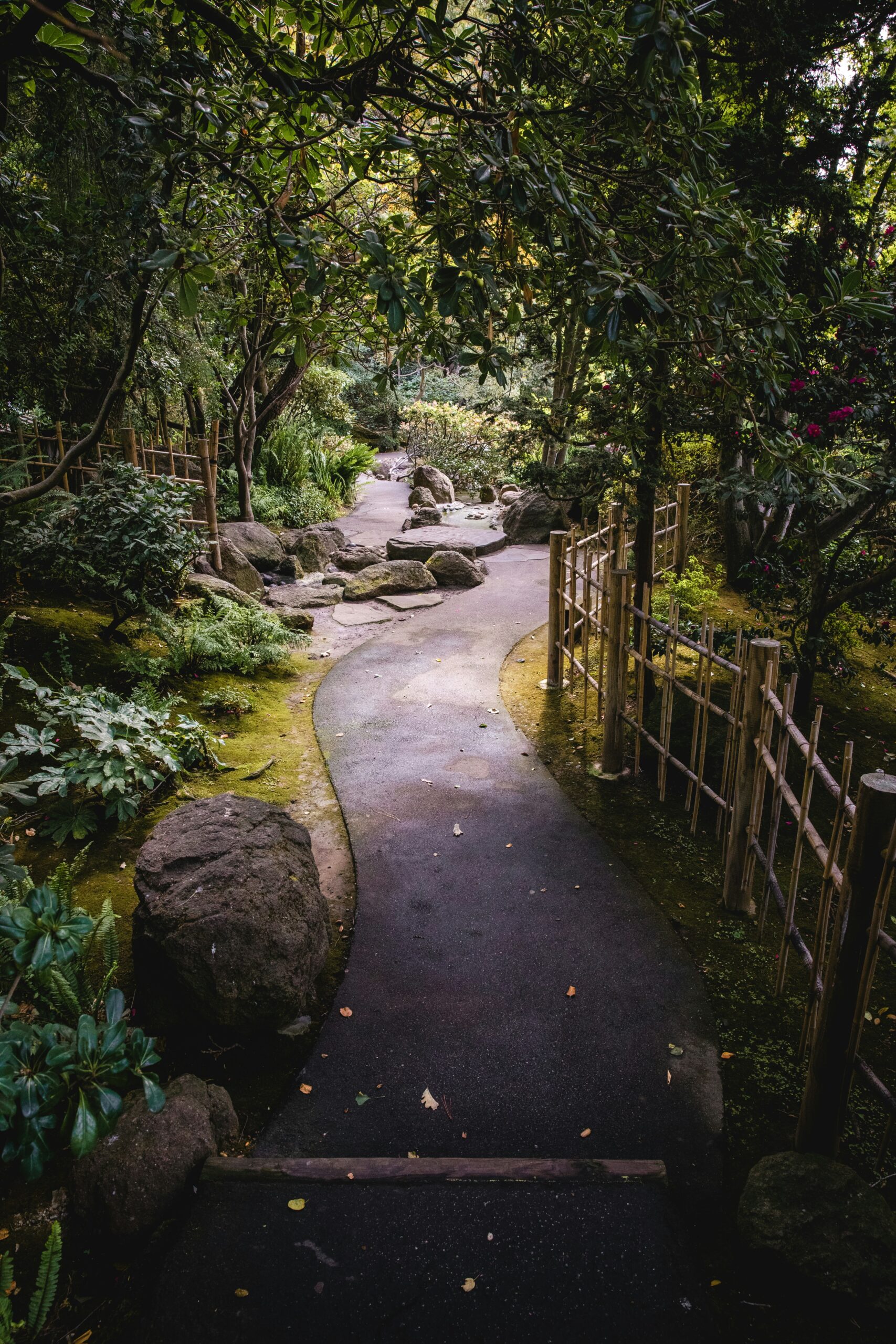 Serene Japanese garden pathway with curved stone bridge, bamboo fencing, lush greenery, and traditional landscaping elements creating perfect natural lighting for kimono photography