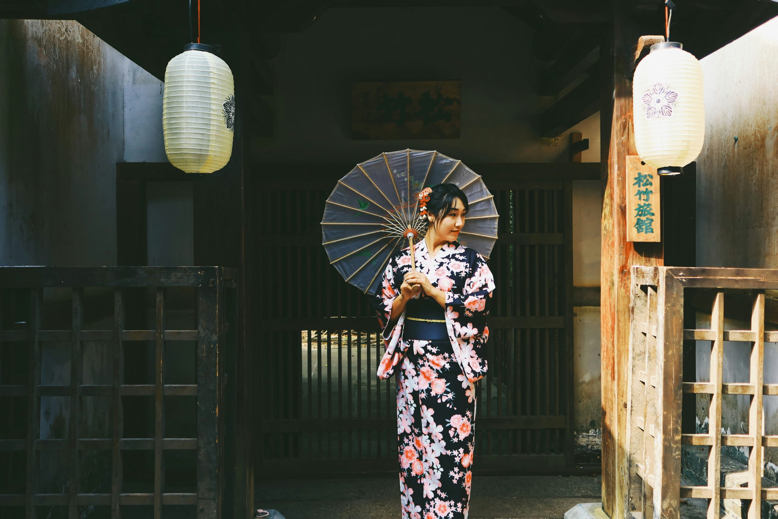 Mujer con kimono floral sosteniendo una sombrilla tradicional frente a un edificio tradicional japonés con linternas de papel, ejemplo perfecto de pose cultural.
