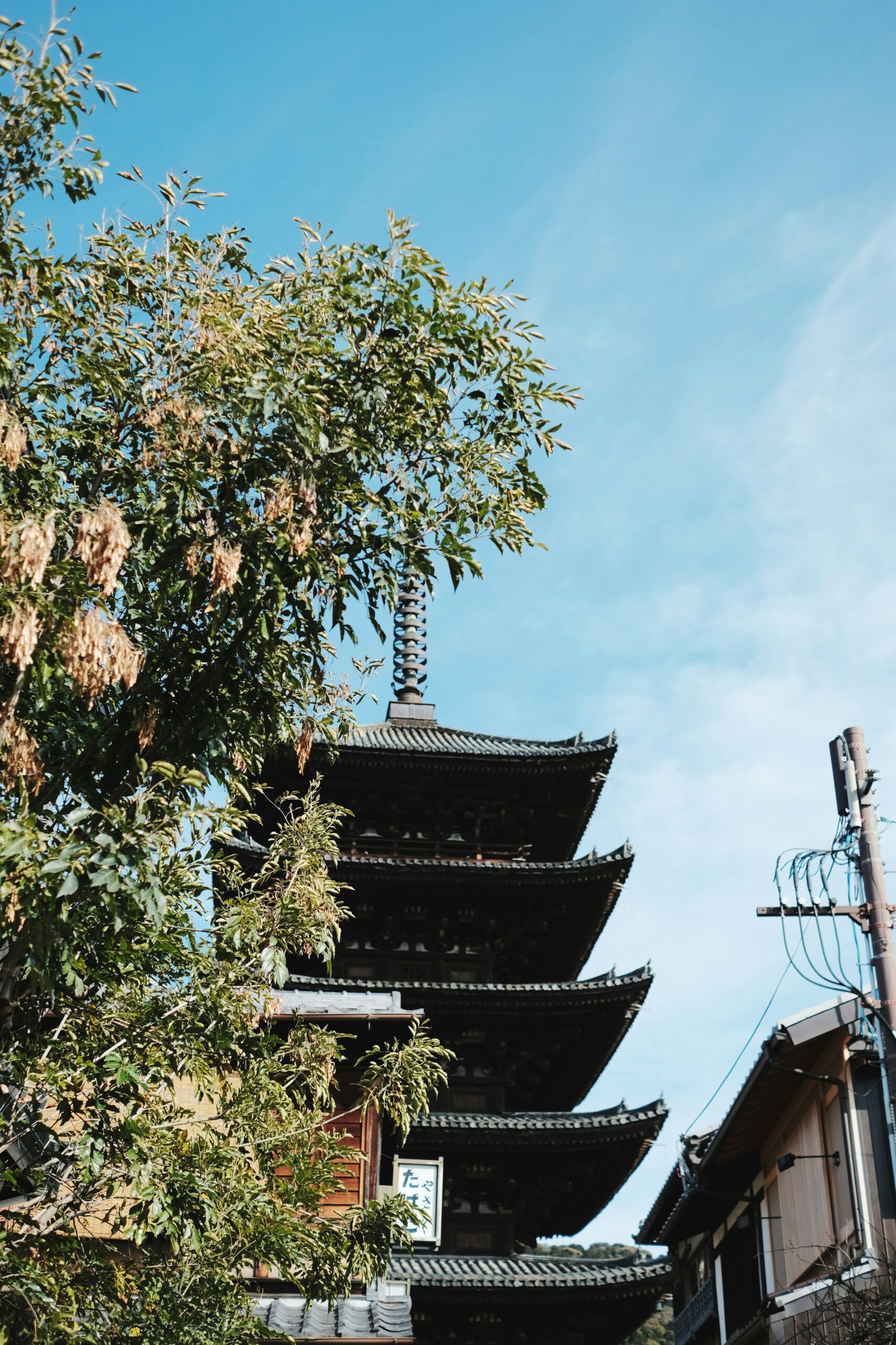 Traditional five-story pagoda in Kyoto with lush green foliage against clear blue sky