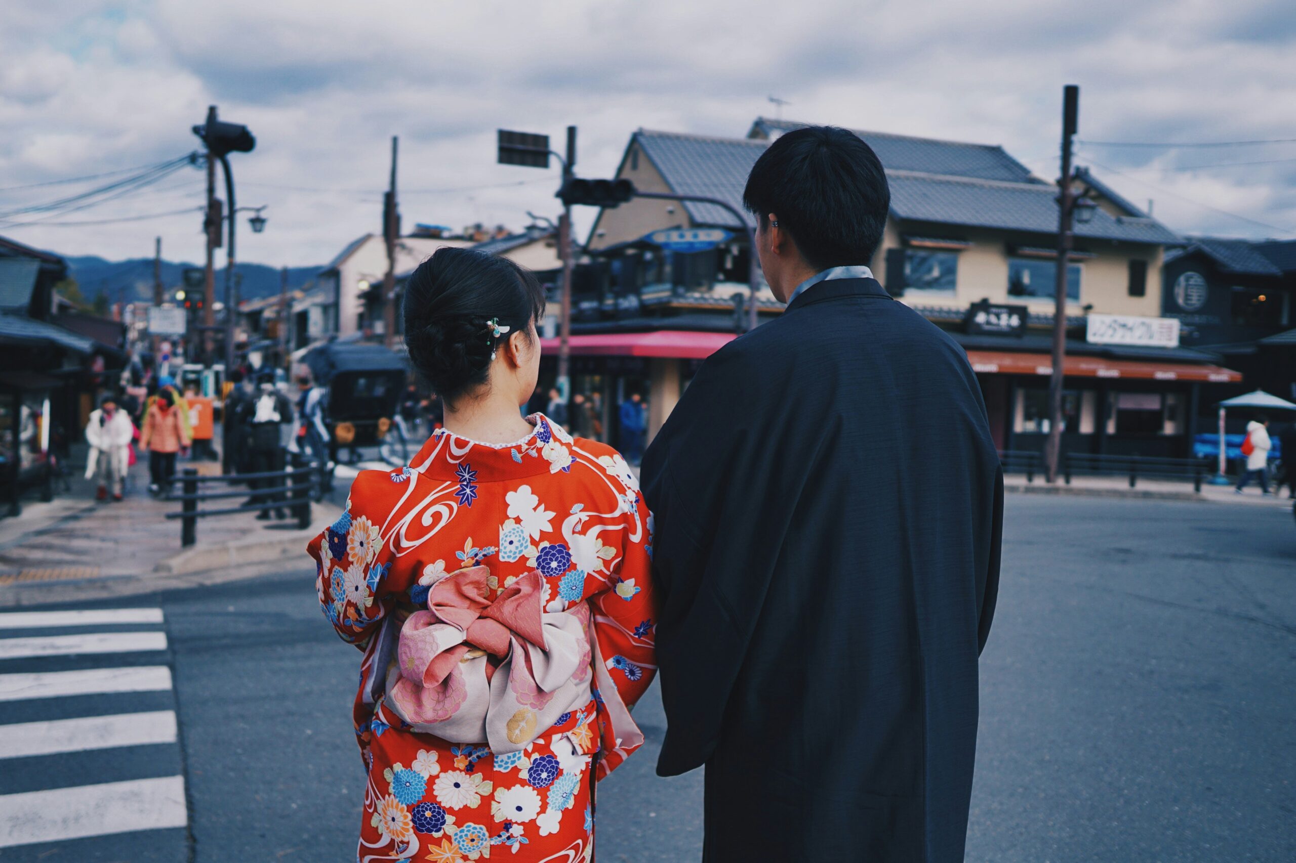 Couple in traditional Japanese attire walking through bustling historic Kyoto street with traditional architecture