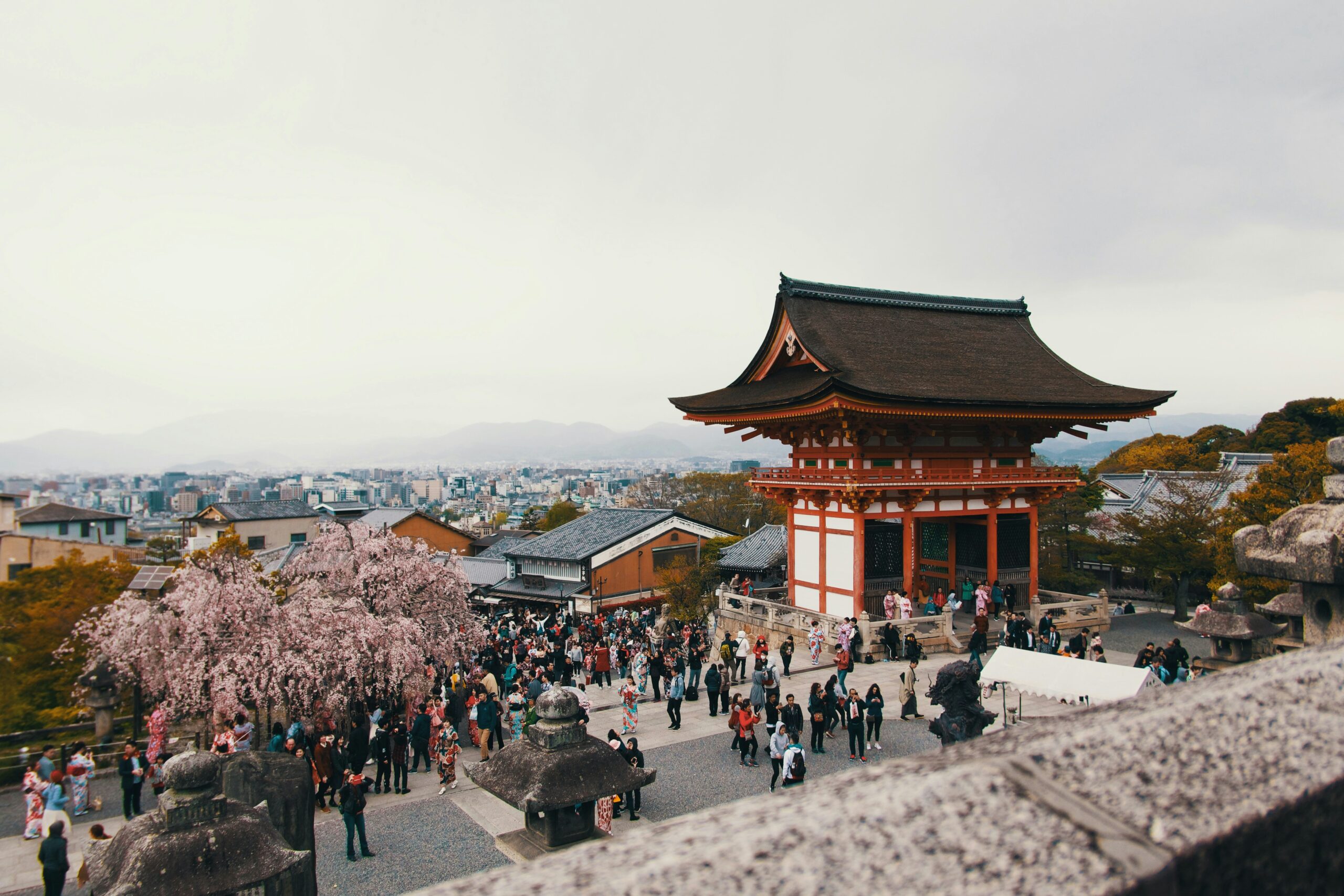 Aerial view of traditional Japanese temple courtyard during cherry blossom season with visitors in kimono attending festival