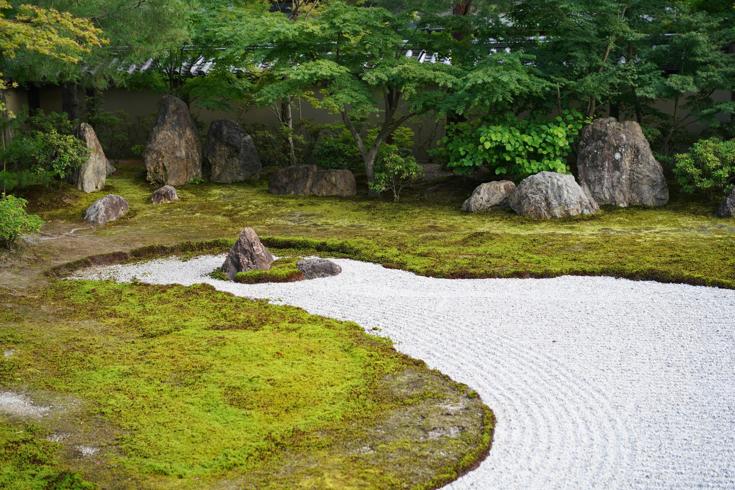 Tranquil Japanese zen garden with raked white gravel and stones surrounded by greenery, representing peaceful meditation spaces