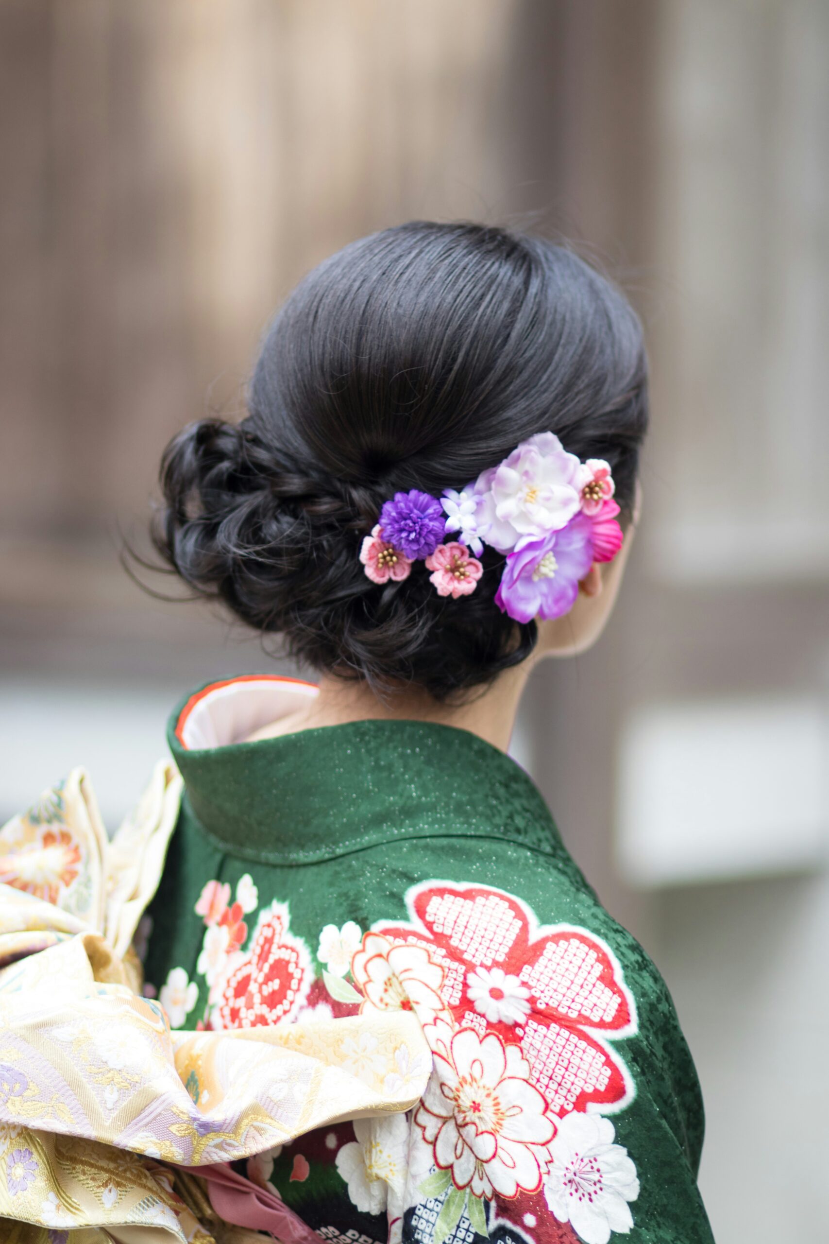 Back view of woman in elaborate kimono with traditional floral hair ornaments, showcasing detailed Japanese cultural dress and styling