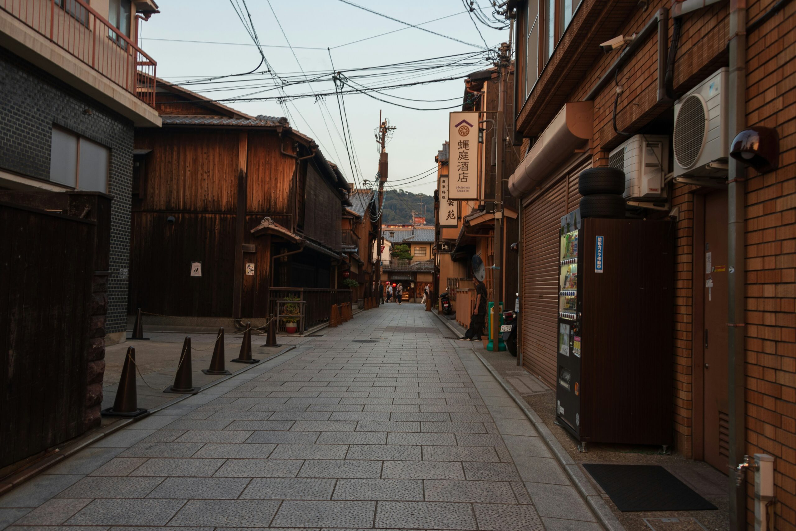 Empty traditional Kyoto street with wooden buildings, stone pavement, Japanese shop signs, and power lines overhead during golden hour, perfect for authentic kimono street photography