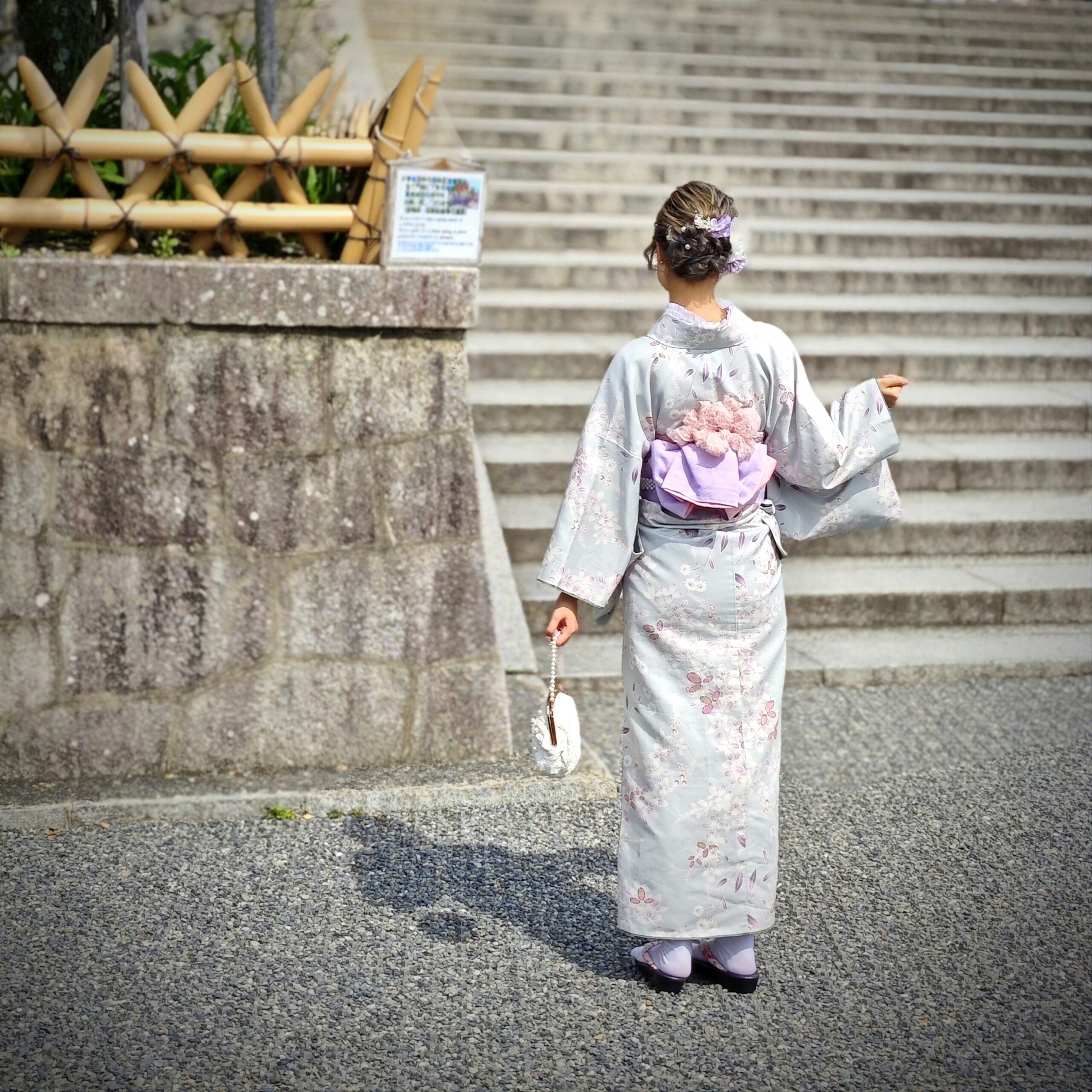 Elegant Japanese woman in traditional pink kimono gracefully climbing stone steps leading to Kiyomizudera Temple in Kyoto, showcasing the authentic cultural experience of visiting sacred sites in traditional dress