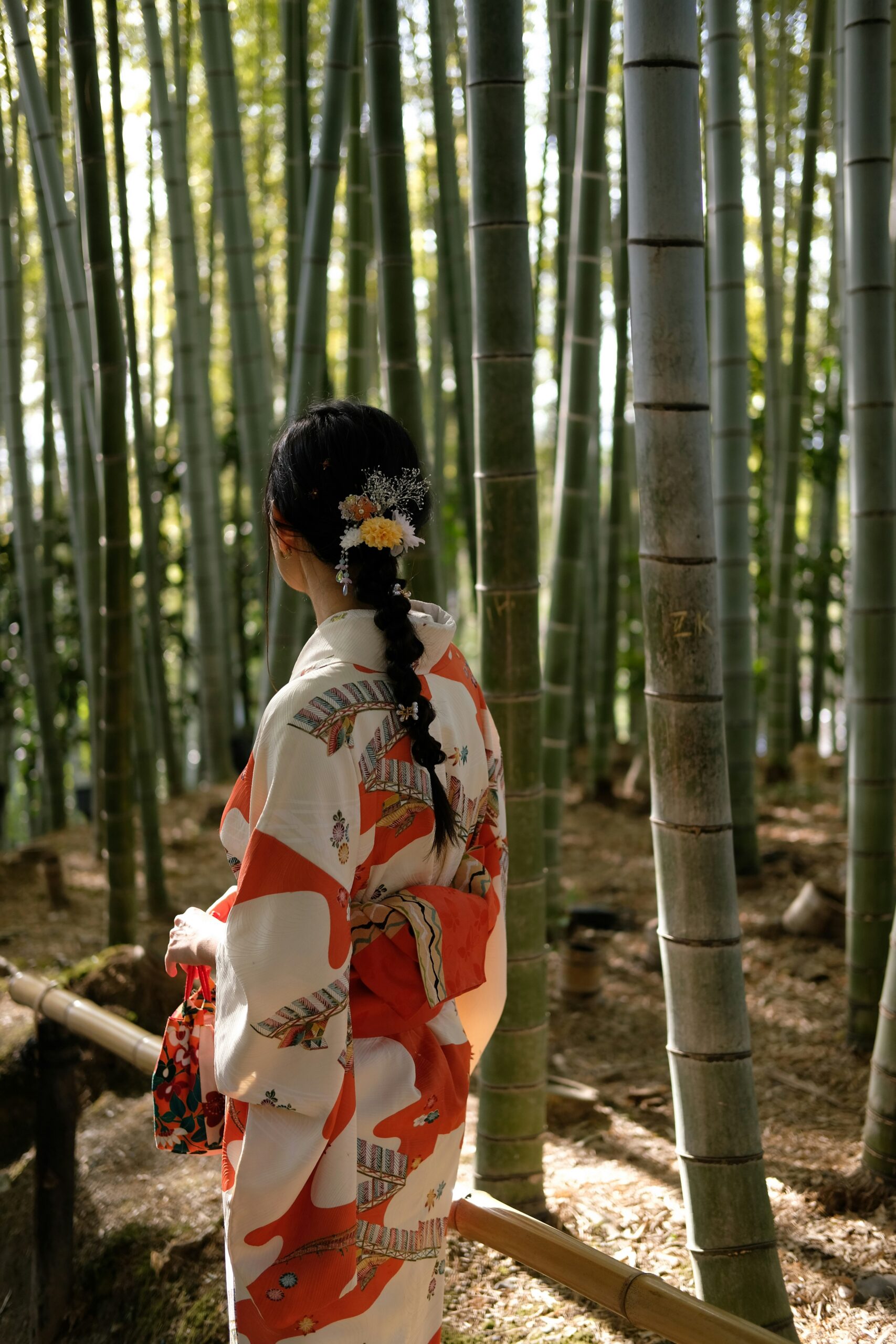 Professional kimono photoshoot in Arashiyama bamboo forest Kyoto featuring woman in traditional Japanese kimono among towering green bamboo stalks with filtered sunlight creating magical atmosphere