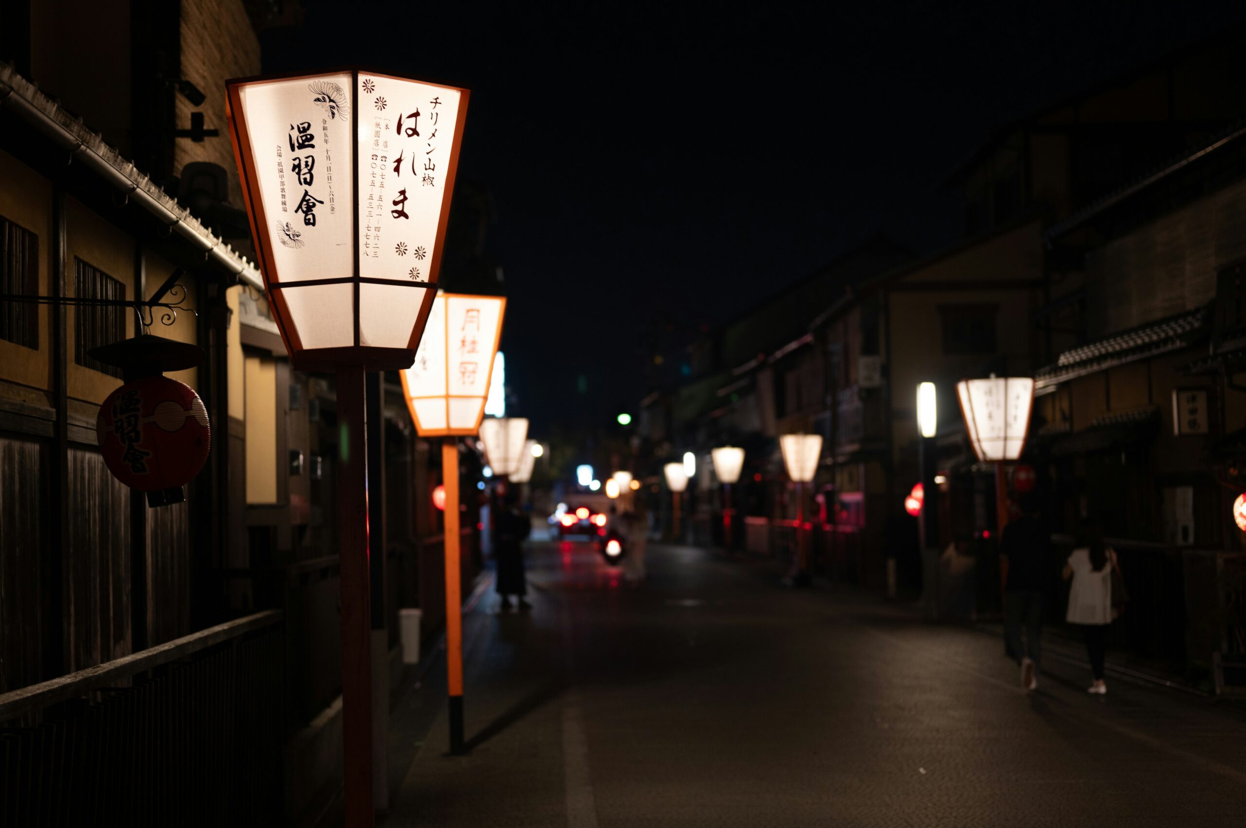 Gion district Kyoto at night with traditional Japanese lanterns illuminating historic streets geisha quarter wooden machiya houses atmospheric evening scene
