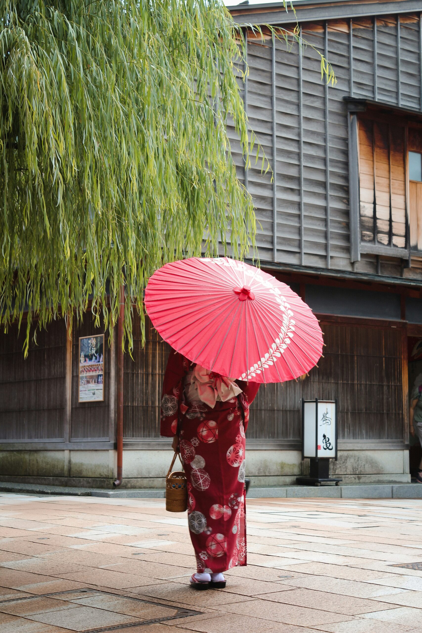 Woman wearing traditional red kimono walking through historic Gion district streets in Kyoto with oil-paper umbrella