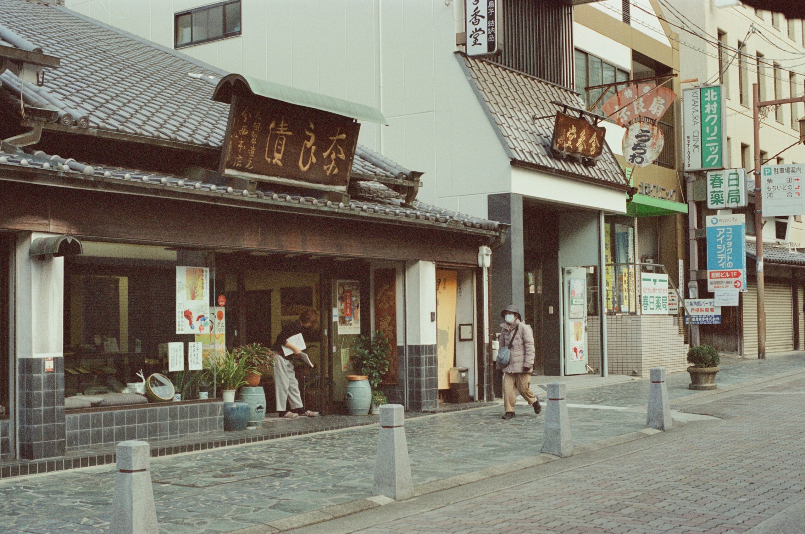 Traditional Japanese onsen town street scene with woman in kimono walking along historic wooden machiya architecture riverside hot spring resort atmosphere peaceful Kyoto countryside cultural heritage